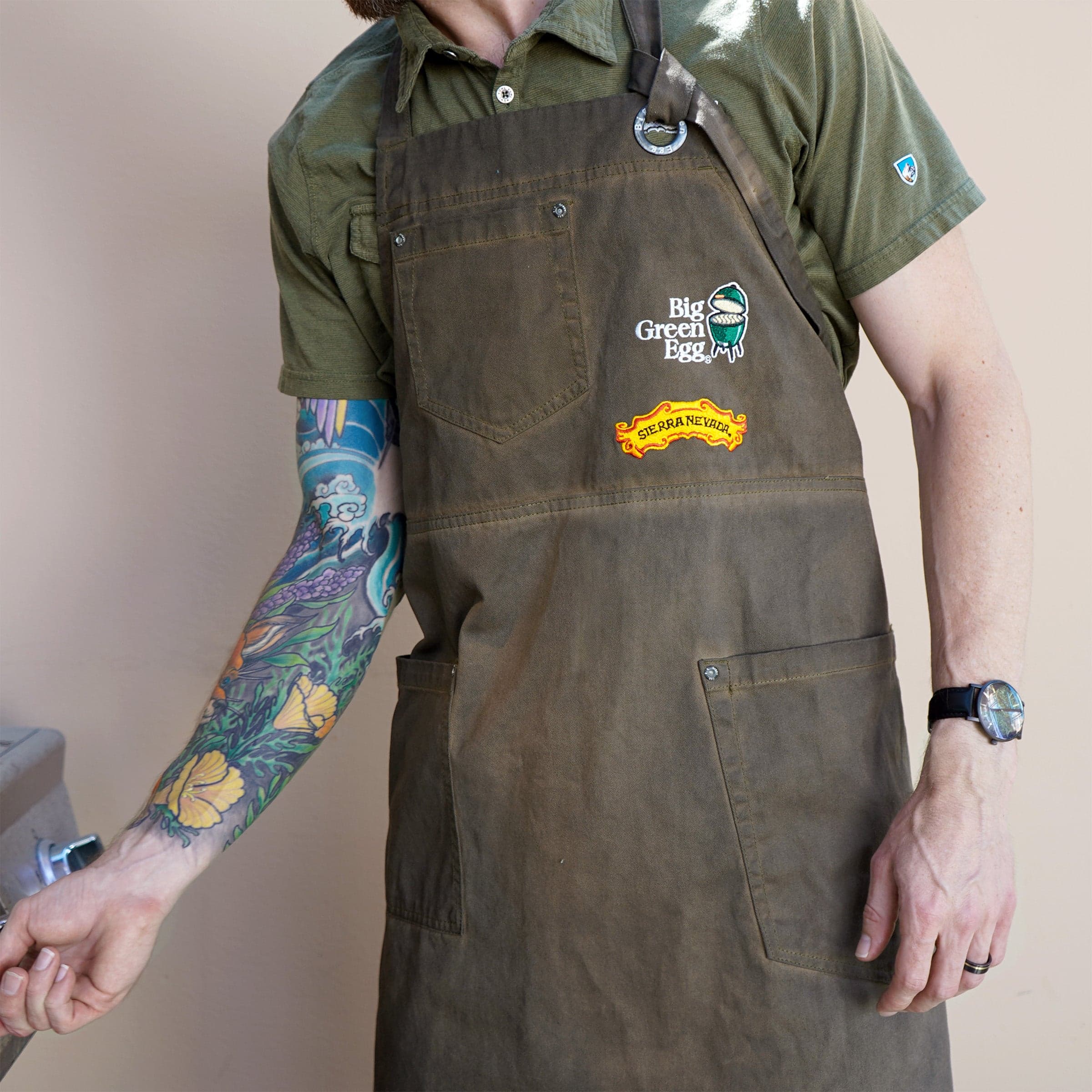 A man wears the Sierra Nevada Big Green Egg Grilling Apron while tending the grill