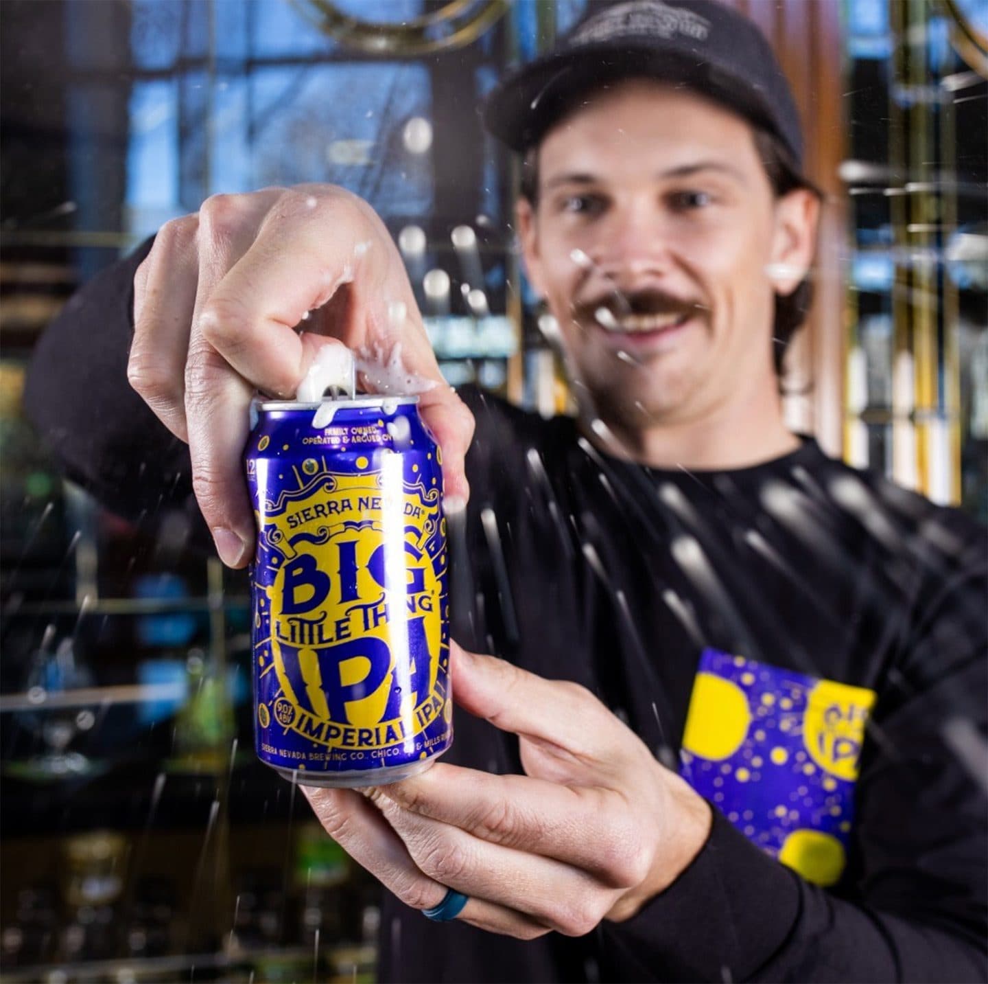 Man in a taproom opening a spraying can of Big Little Thing IPA beer